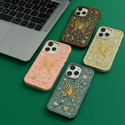 Four phone cases with butterfly designs on a green surface next to a laptop.