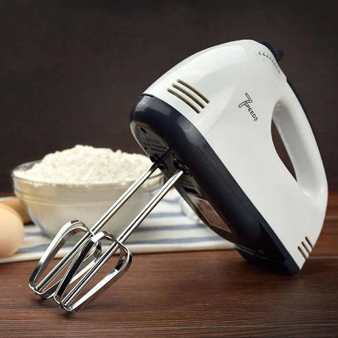 Hand mixer on a wooden surface with a bowl of flour and an egg in the background. Emiravaly uae