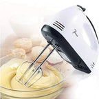 Hand mixer with beaters in a bowl of cream, with cookies in the background Emiravaly uae