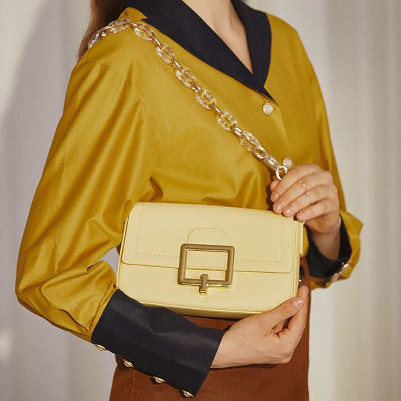 Person holding a yellow handbag with a gold chain strap against a neutral background. Emiravaly