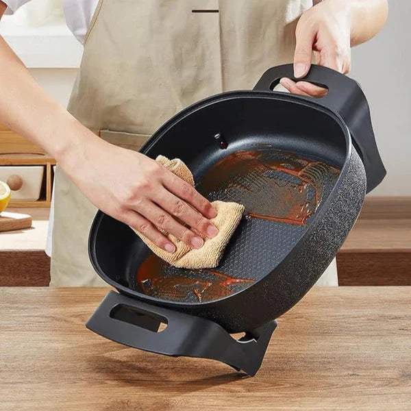 Person cleaning a black frying pan with a sponge on a wooden surface, text indicating ease of cleaning.